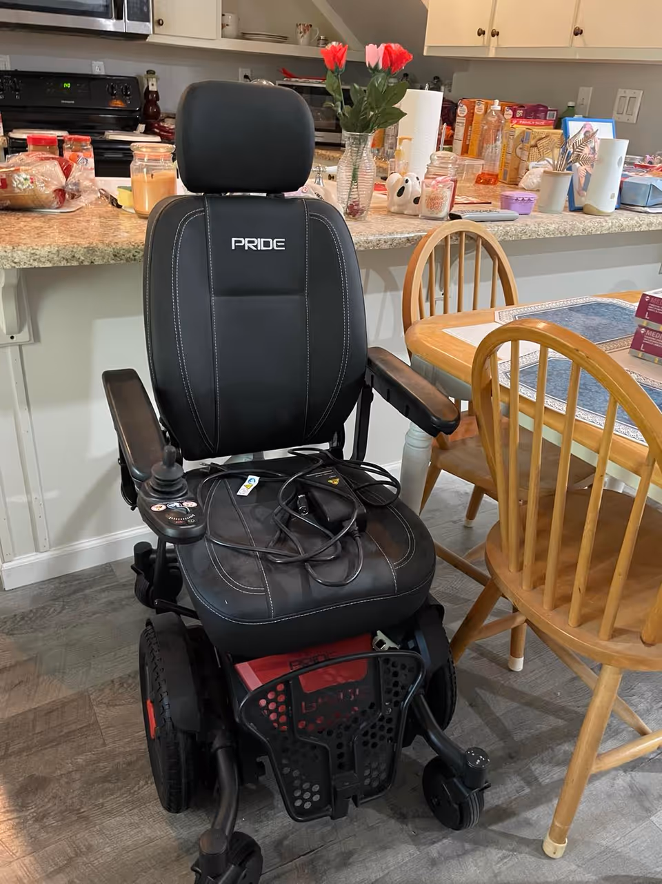 A black Pride power wheelchair sits in a kitchen and dining area.