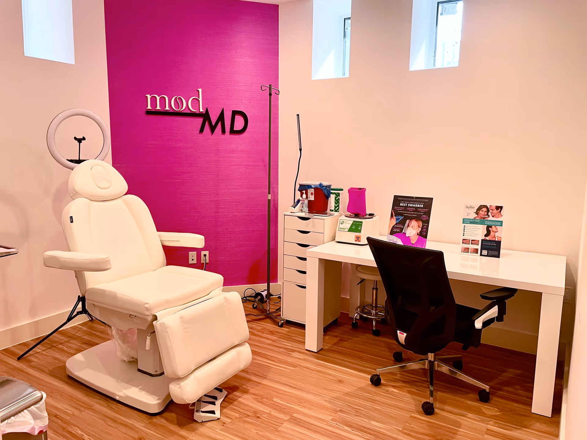 Bright clinic treatment room with a white reclining chair and pink accent wall.