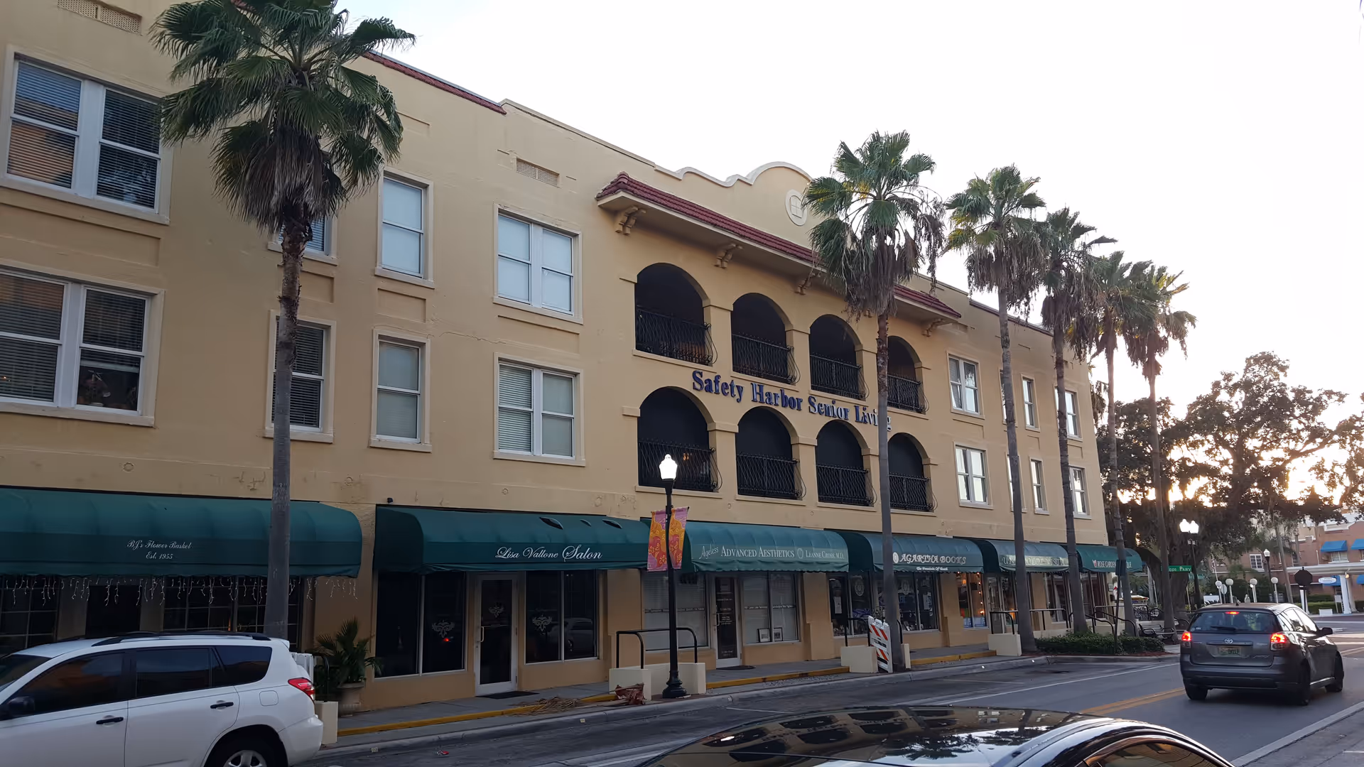 Exterior of Safety Harbor Senior Living building with arches, palm trees, and storefront awnings.