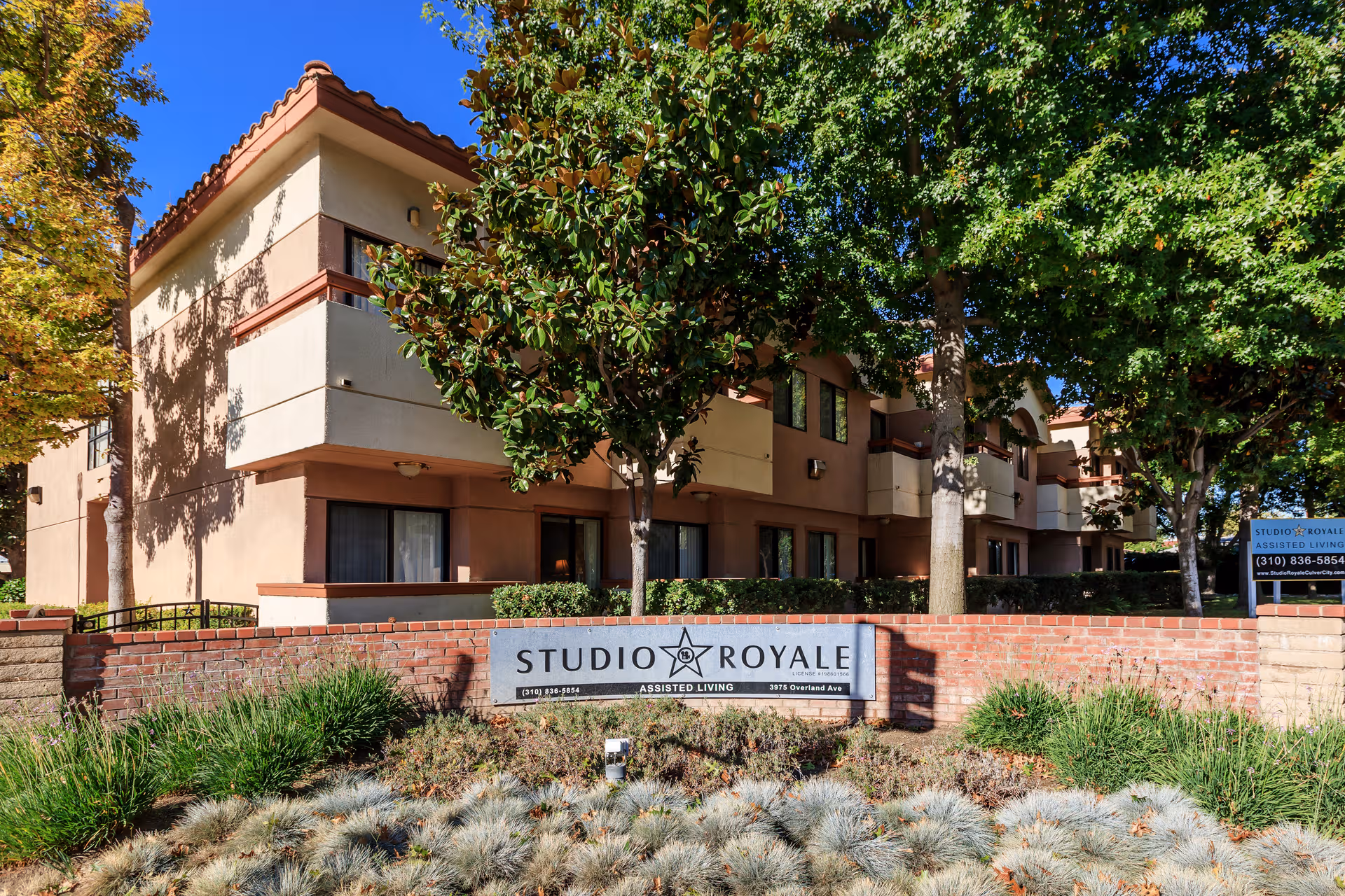 Exterior view of Studio Royale senior living building with sign and trees.