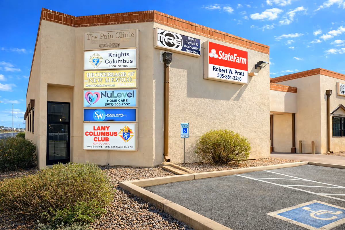 Exterior view of a beige commercial building with multiple business signs and parking.