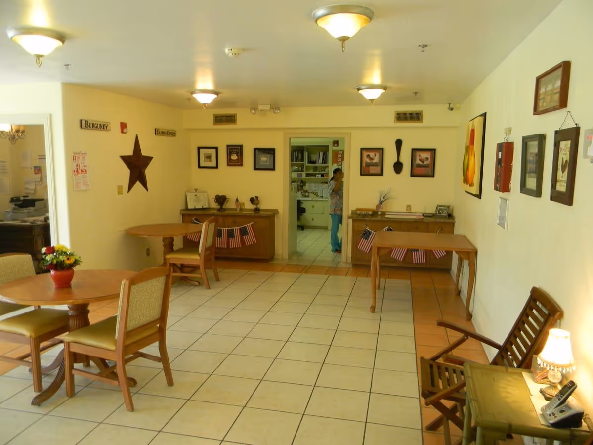 Well-lit senior living dining area with round tables, chairs, and wall art.