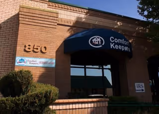 Brick building entrance with blue canopy reading Comfort Keepers and 850 street number.