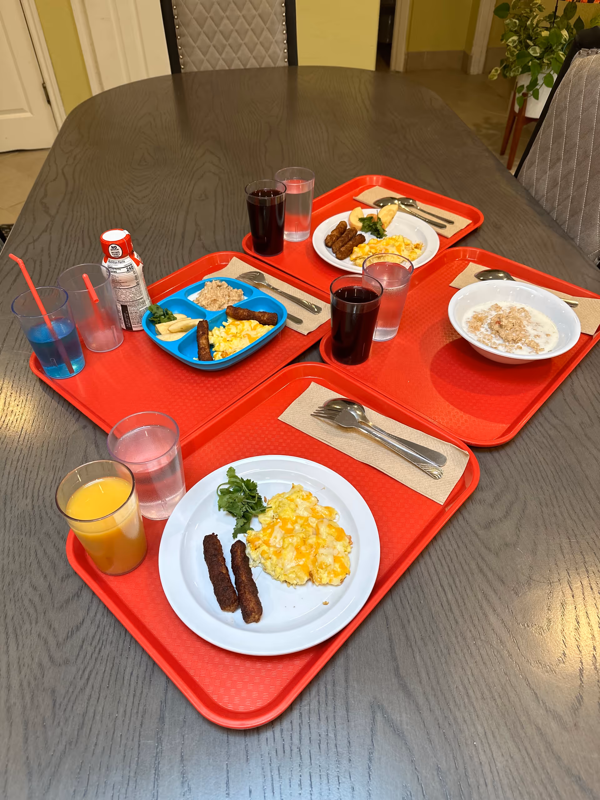 Several red-trayed meals and drinks arranged on a dining room table.