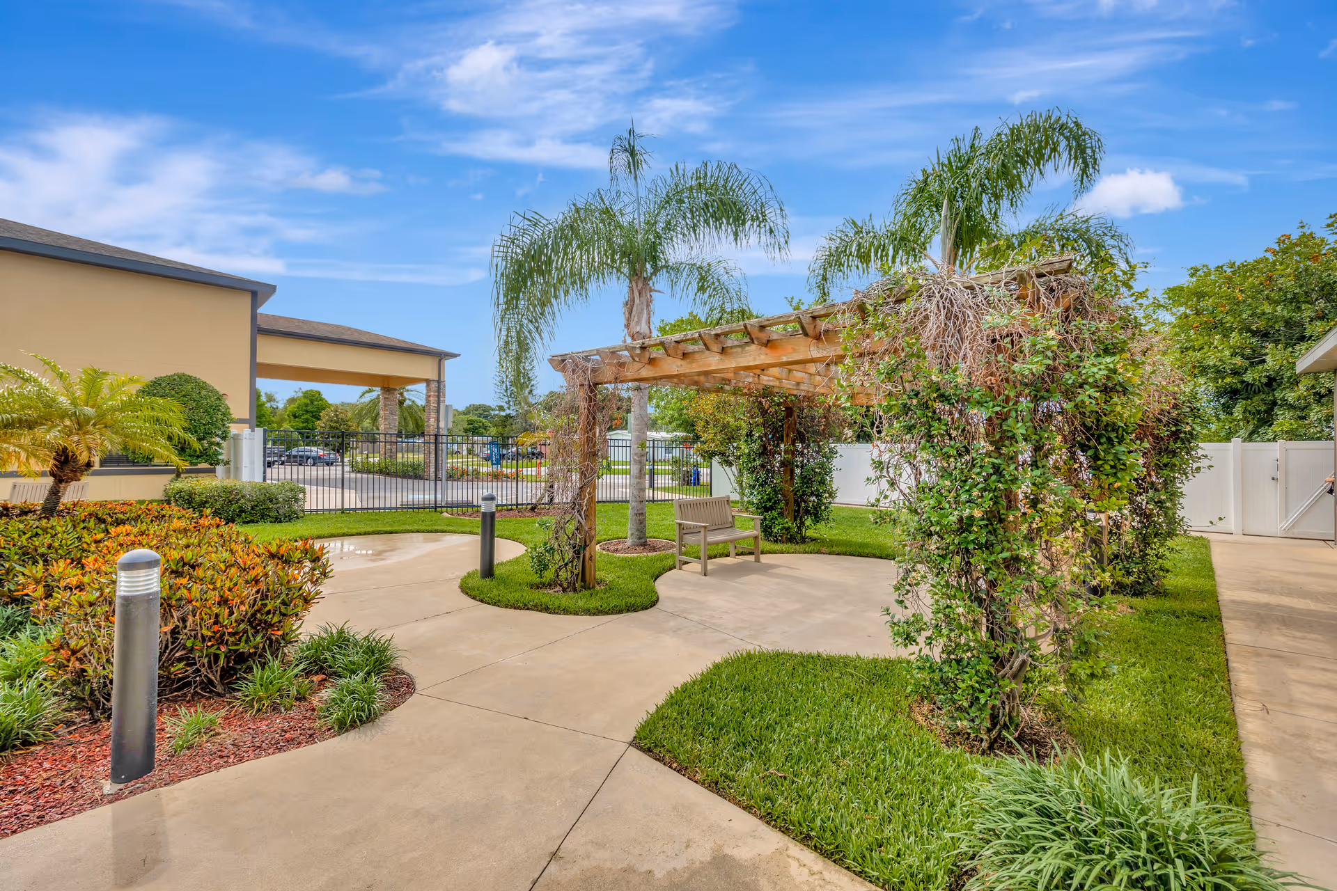 Outdoor courtyard with pergola, bench, and palm trees along walkways.