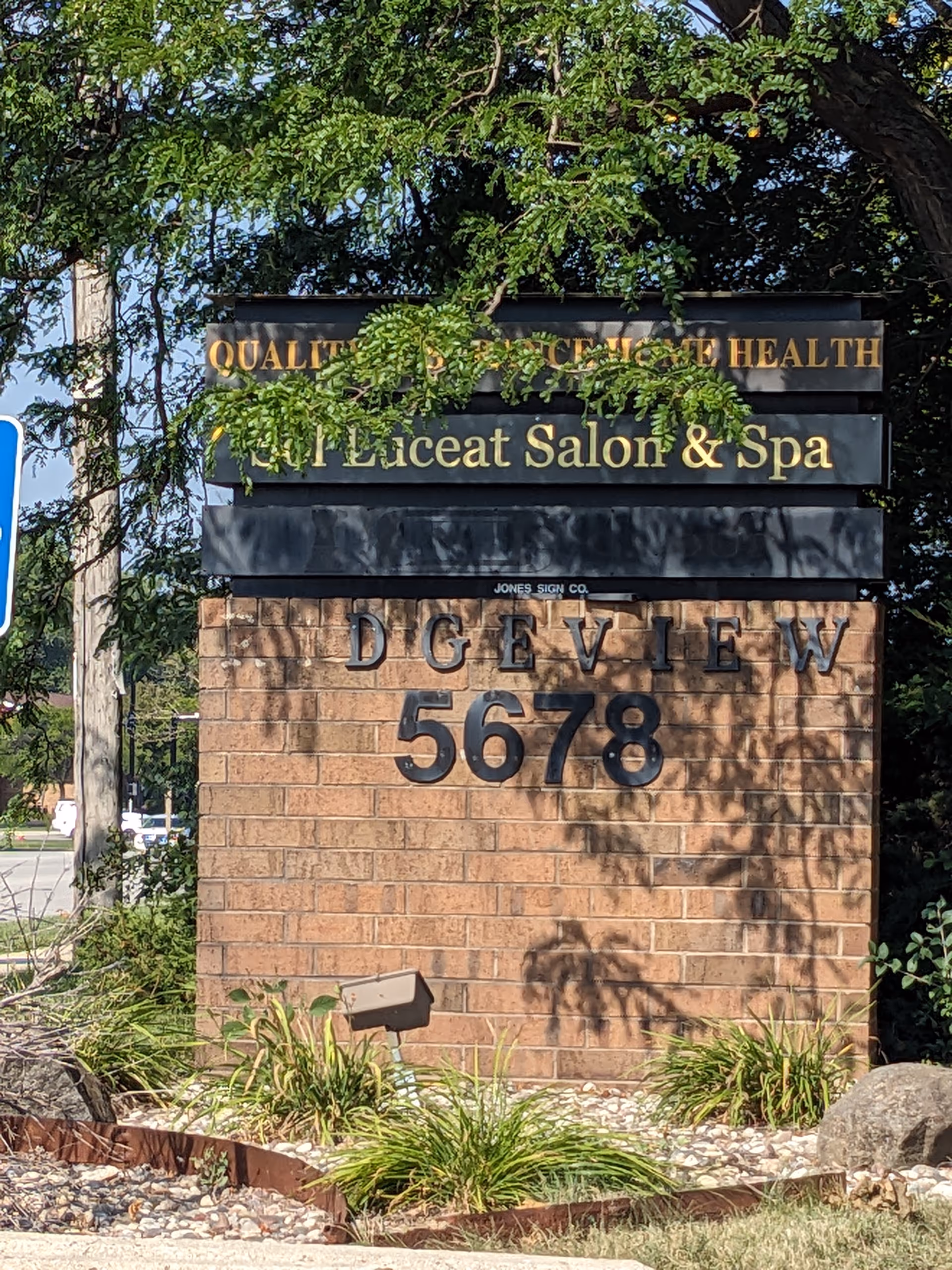 A brick sign with gold lettering reading Quality Assurance Health and Salon and Spa outdoors.