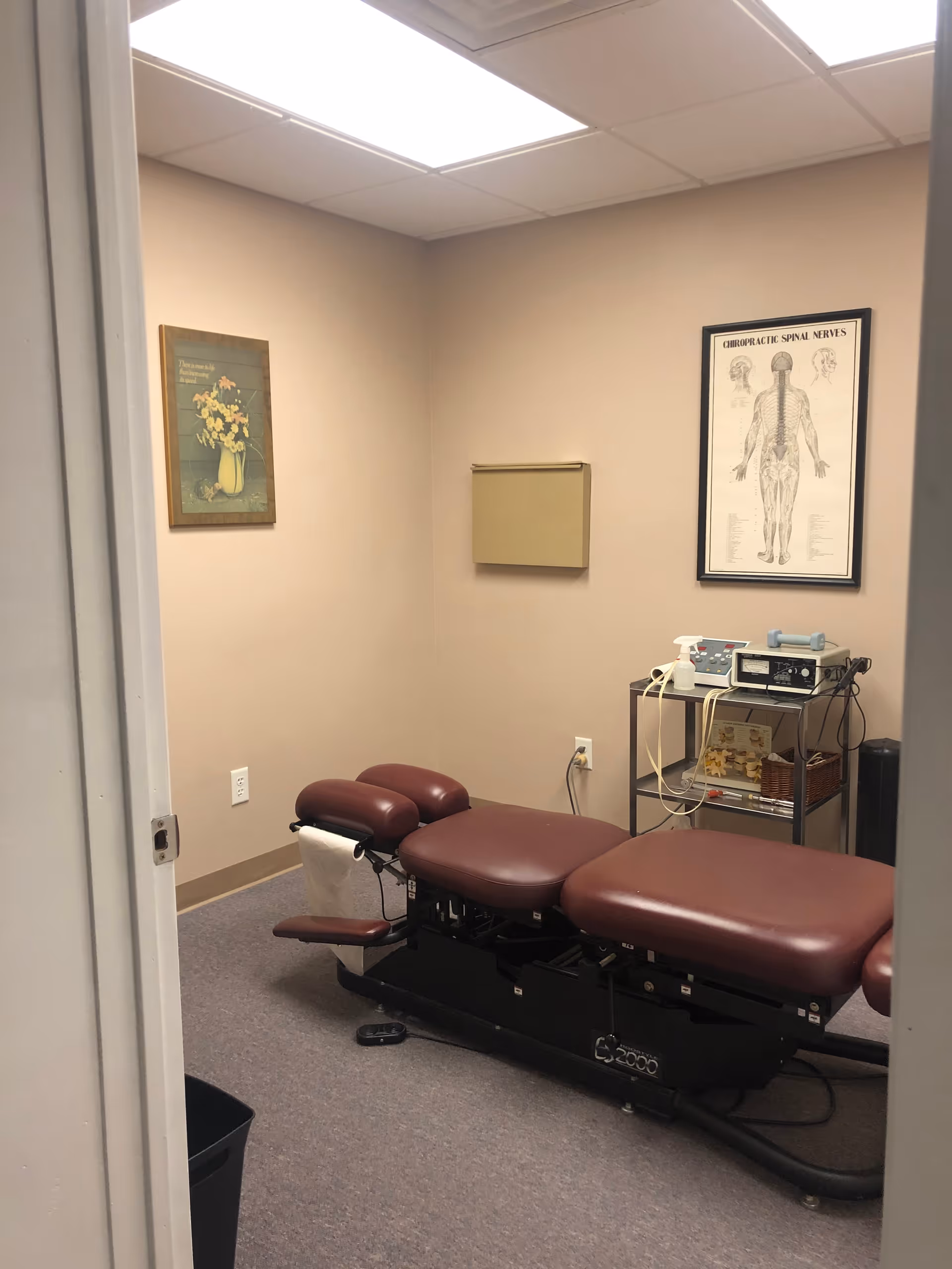 A chiropractic examination room with a burgundy table and equipment cart.