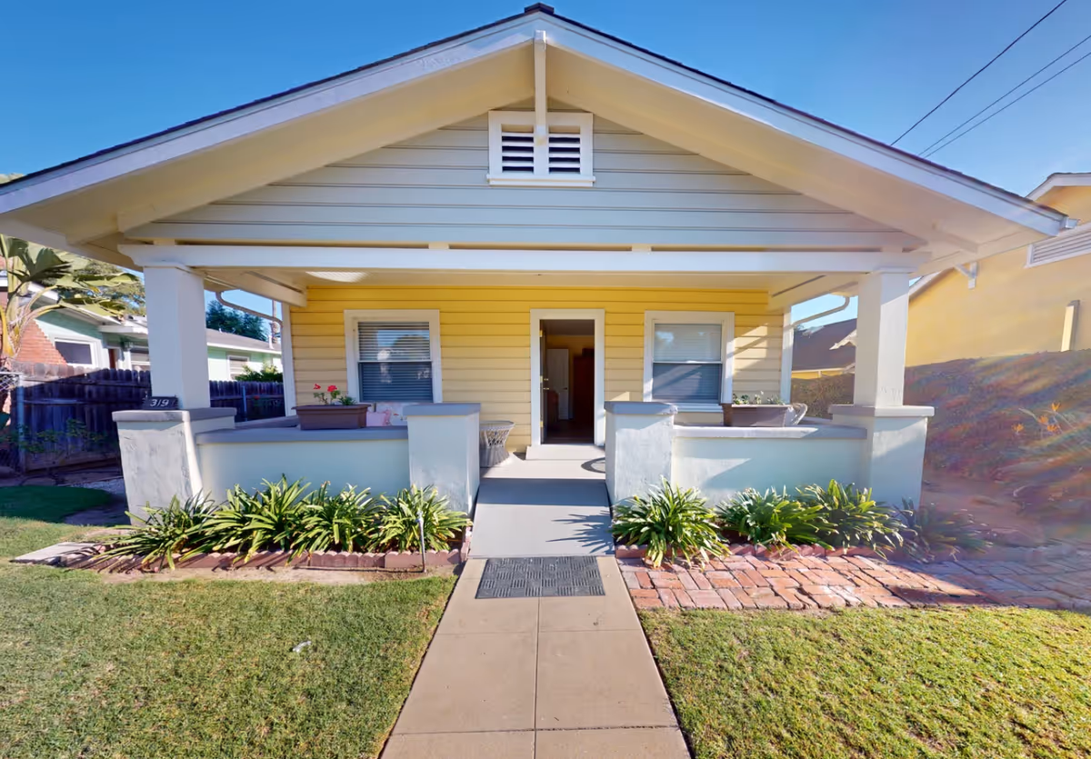 Yellow bungalow-style senior living front porch with planters and a walkway