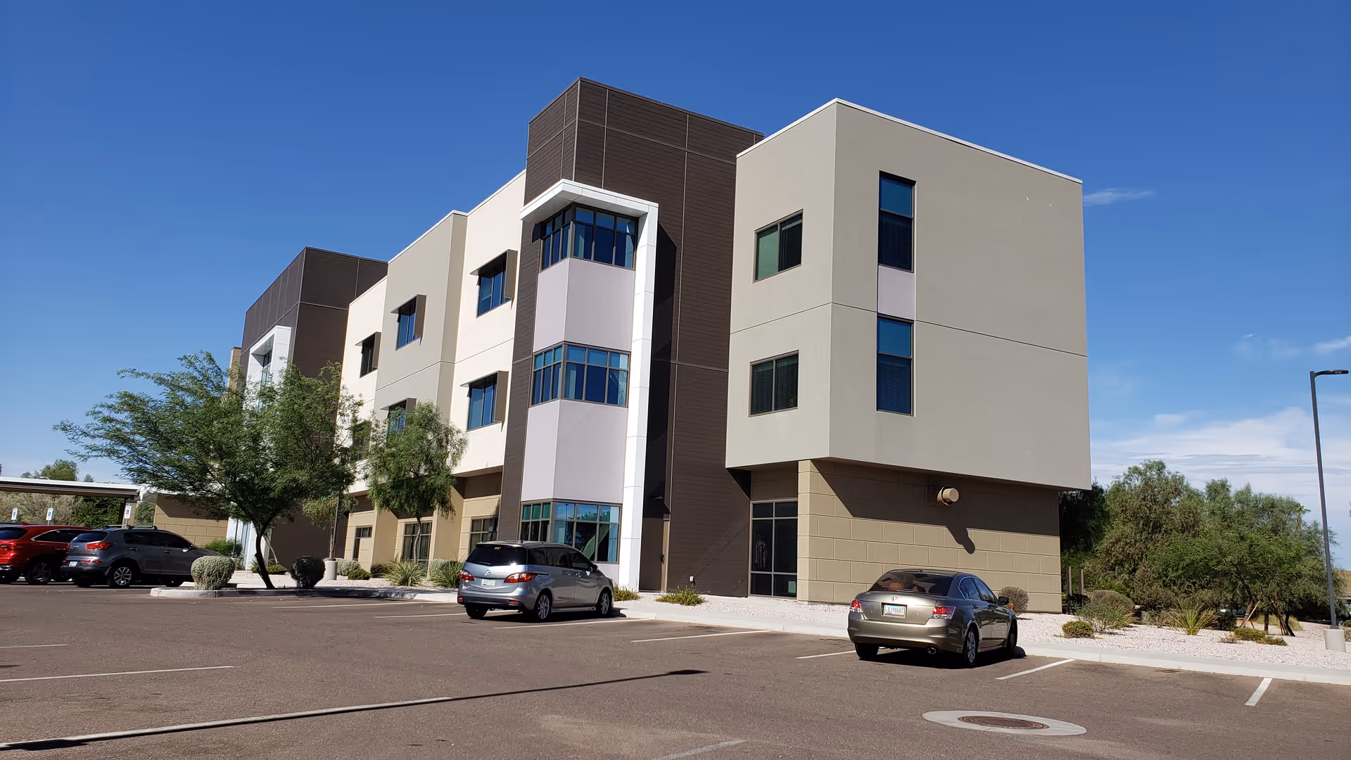 Modern senior living facility with multiple beige and brown facade, parking lot, and blue sky.