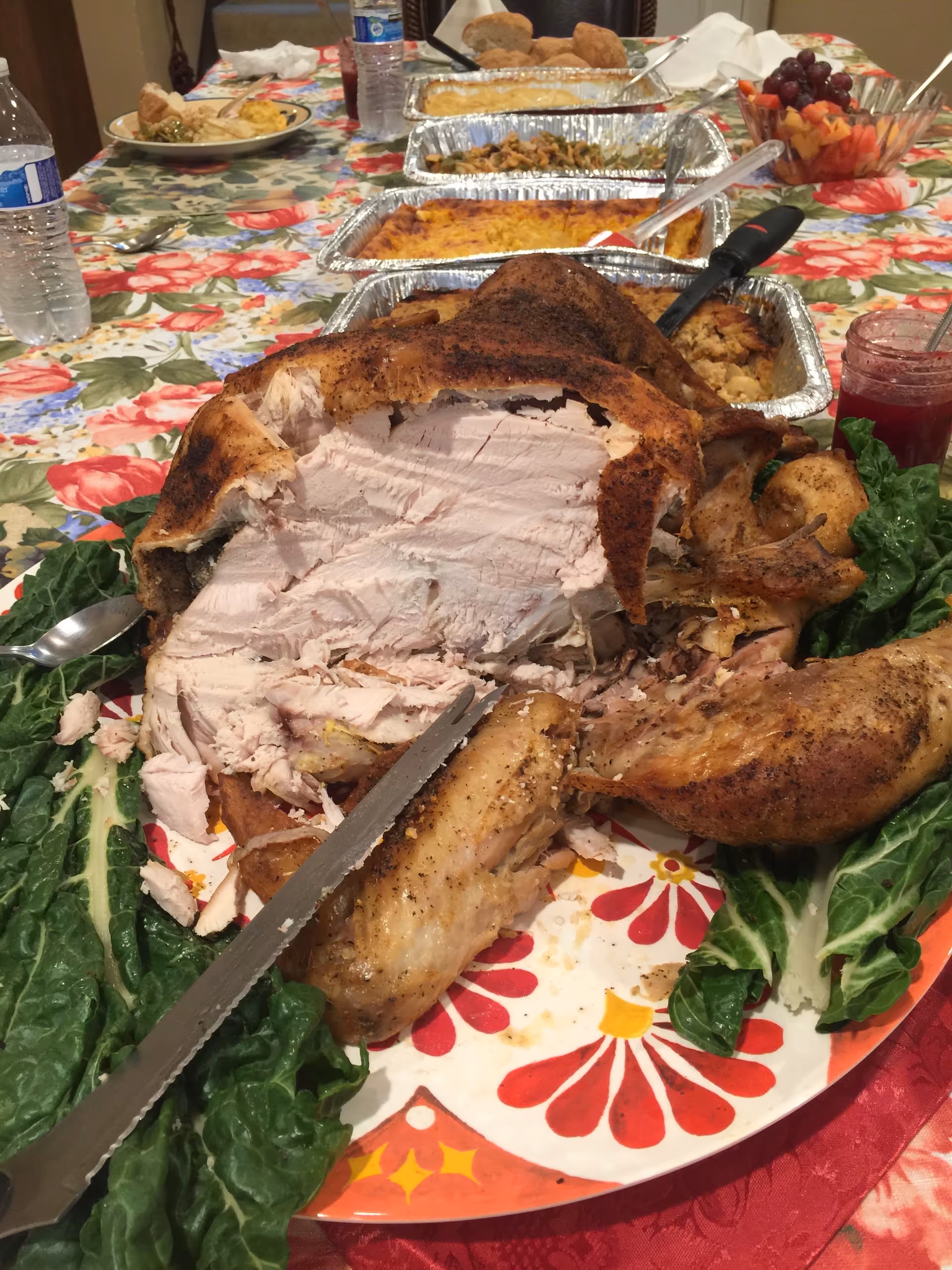 A carved roasted turkey with sides on a floral tablecloth dining table.