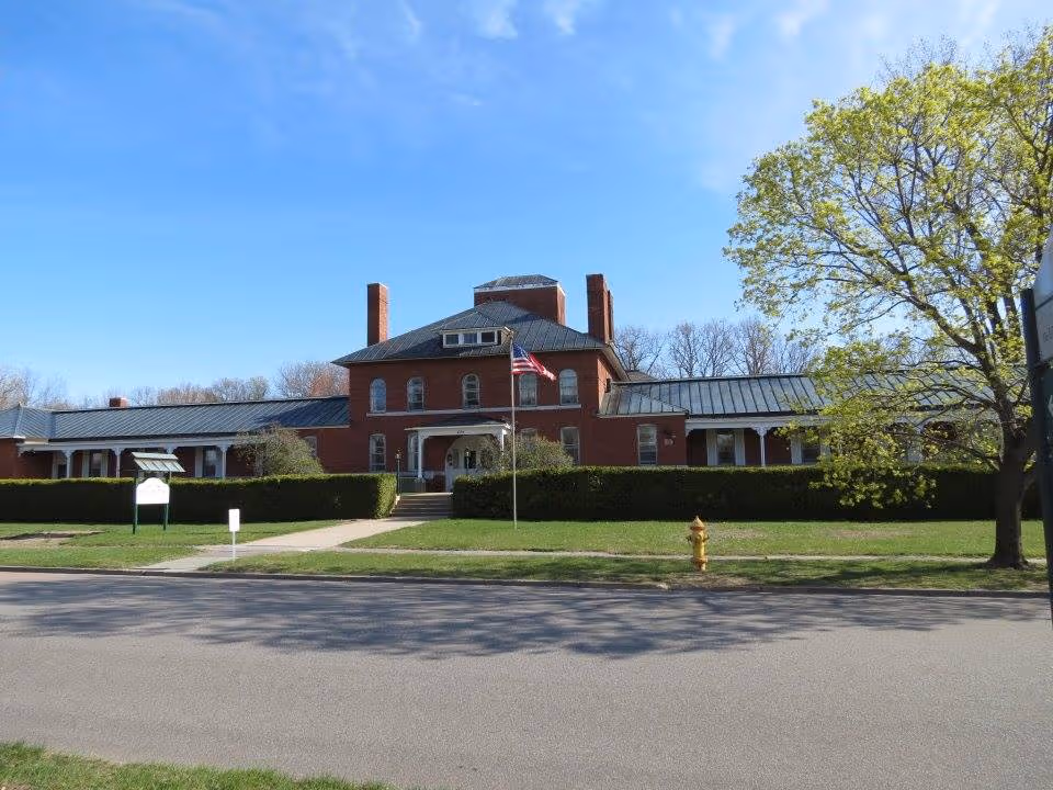 Brick nursing home building with flagpole, manicured lawn, and blue sky in front view.