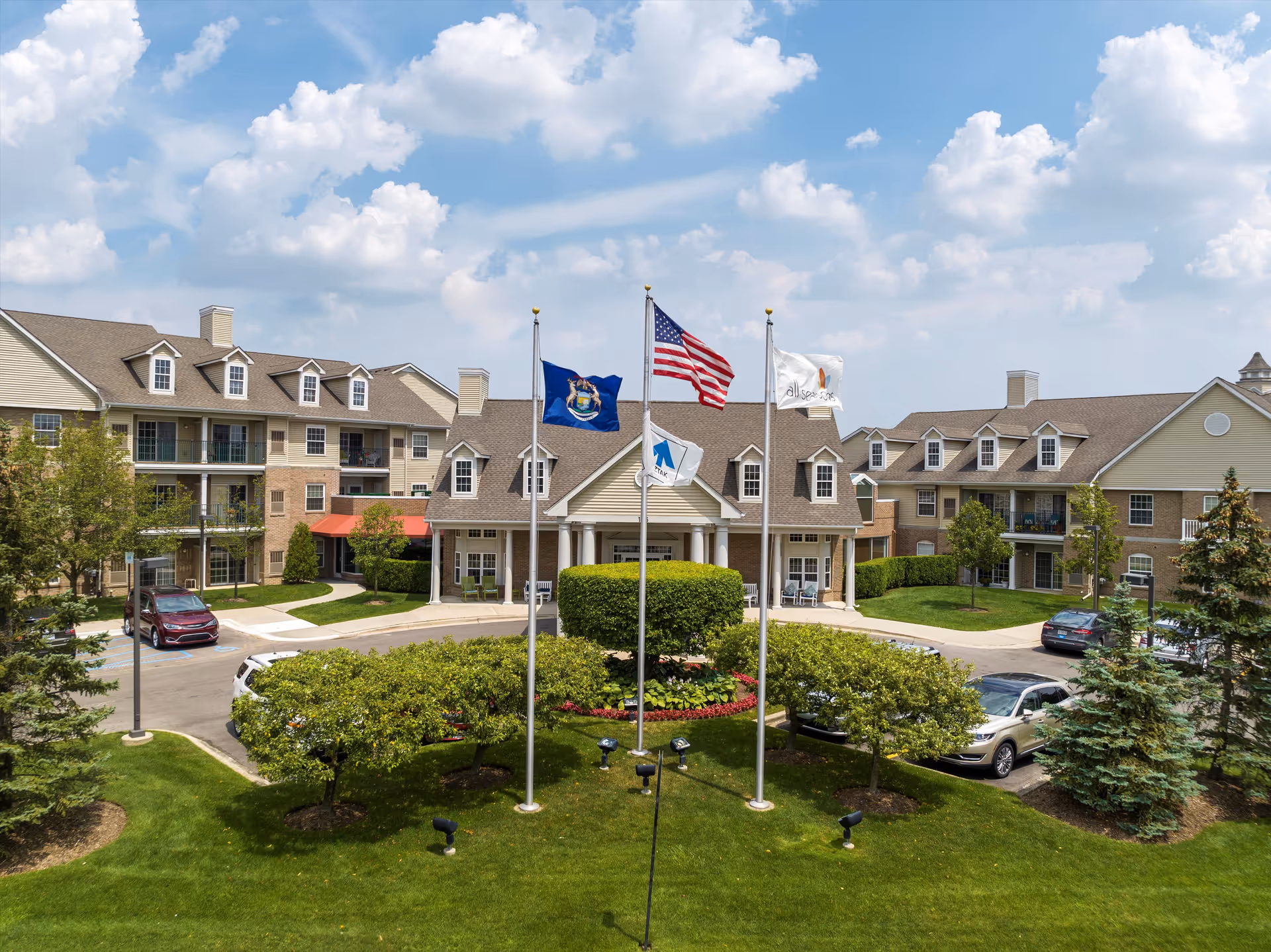 Exterior view of All Seasons Rochester Hills senior living with flagpoles and landscaped grounds.