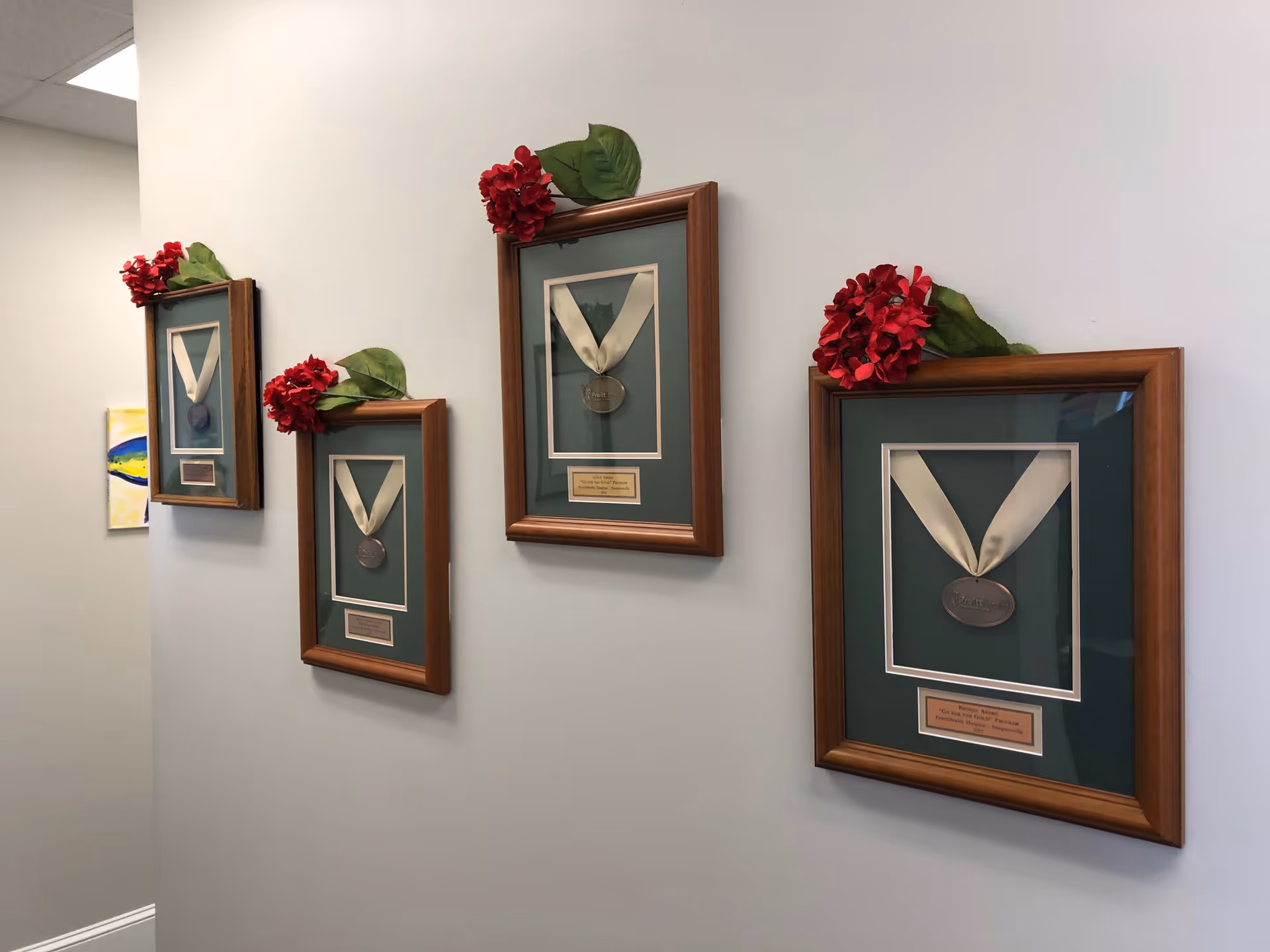 Hallway wall displaying framed medals with red flowers atop each frame.