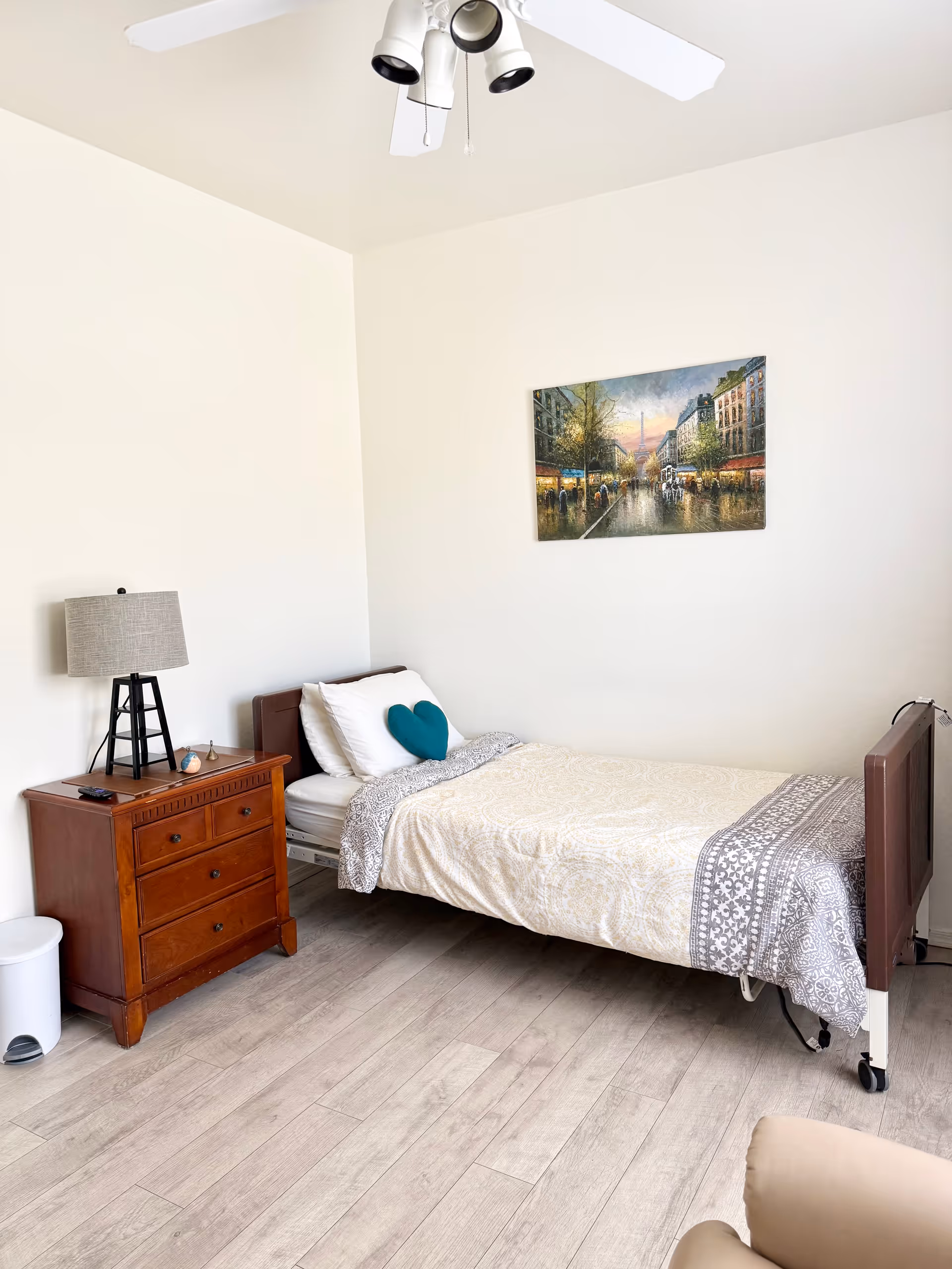 Bedroom in Crystal Rose facility featuring a single bed, dresser, lamp, and wall art.