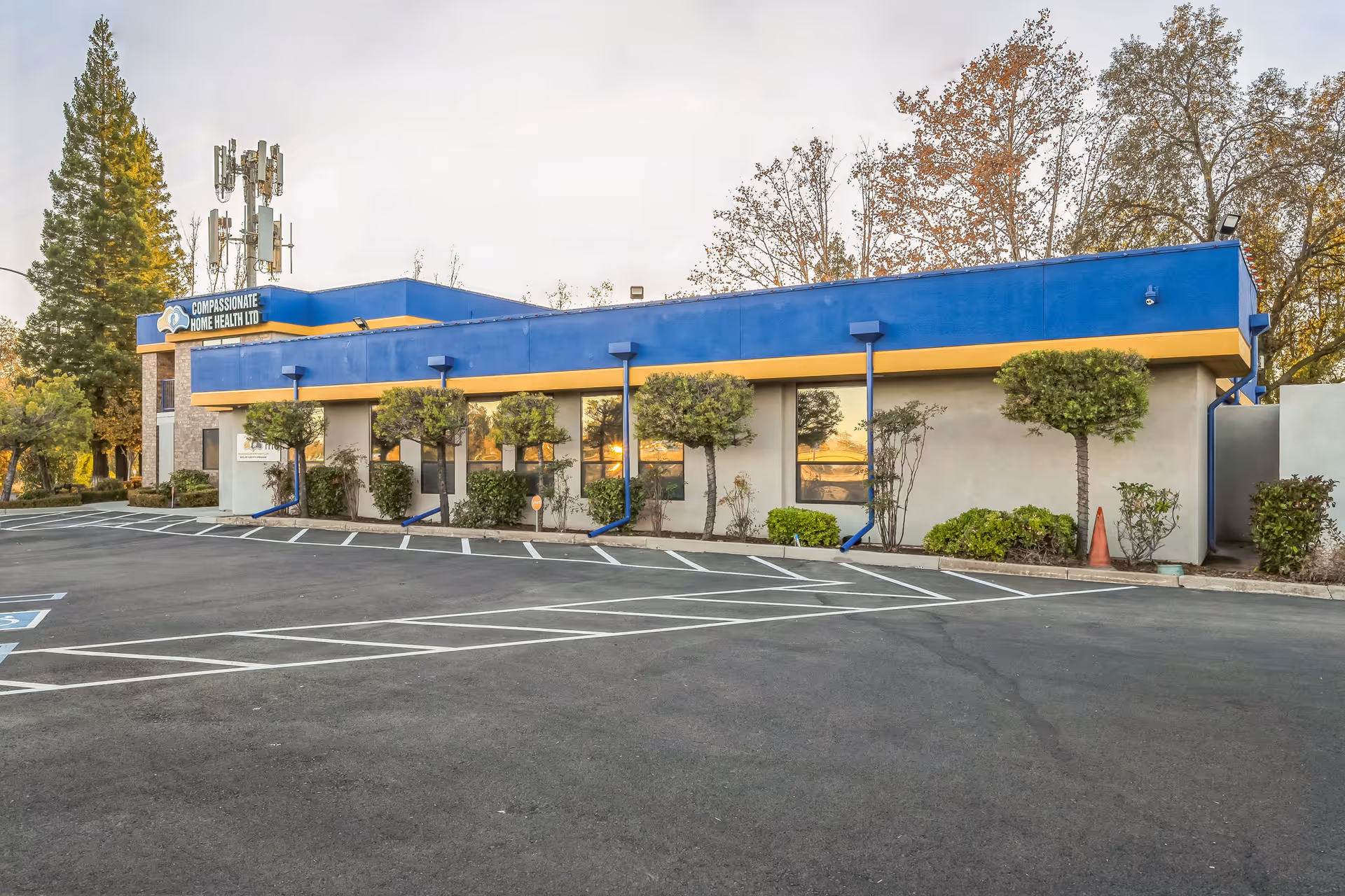 Blue and yellow single-story facility exterior with Compassionate Home Health Ltd sign and parking.
