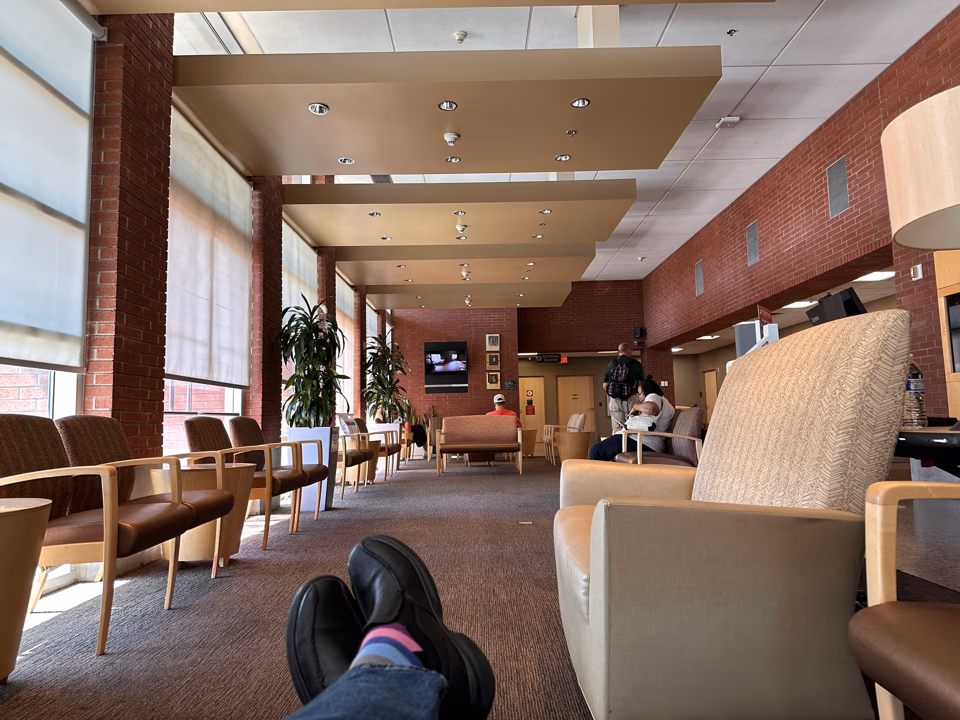 Bright interior hospital lobby with rows of chairs and a few people seated.