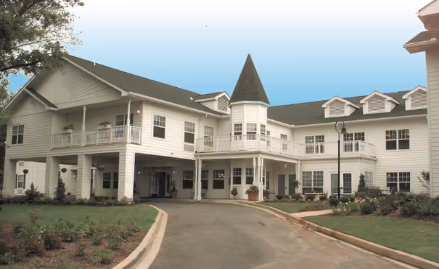 Exterior view of a white multi-wing senior living building with balconies and a curved driveway.