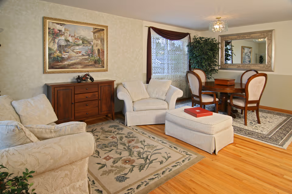 A cozy living room in a senior facility with sofas, chairs, and a dining area.