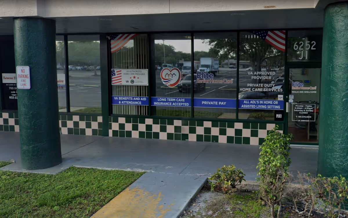 Exterior view of Elite Senior Home Care storefront with glass doors, banners, and flags.
