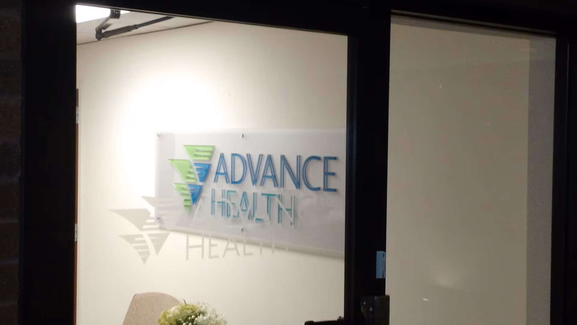 Interior lobby area with a backlit Advance Health sign on the wall.