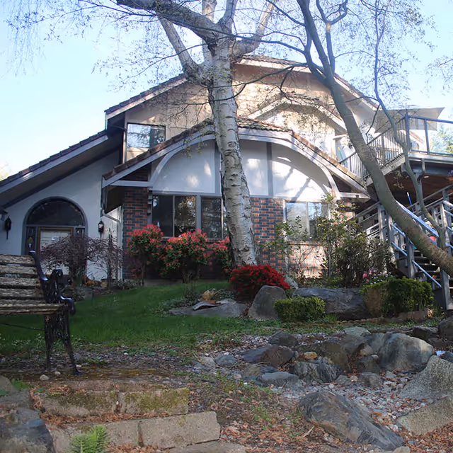 Front exterior of a two-story house with brick and beige siding, surrounded by trees.