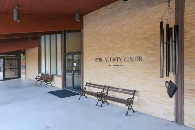 Covered entrance to the Byer Activity Center showing a brick facade, benches, and glass doors.