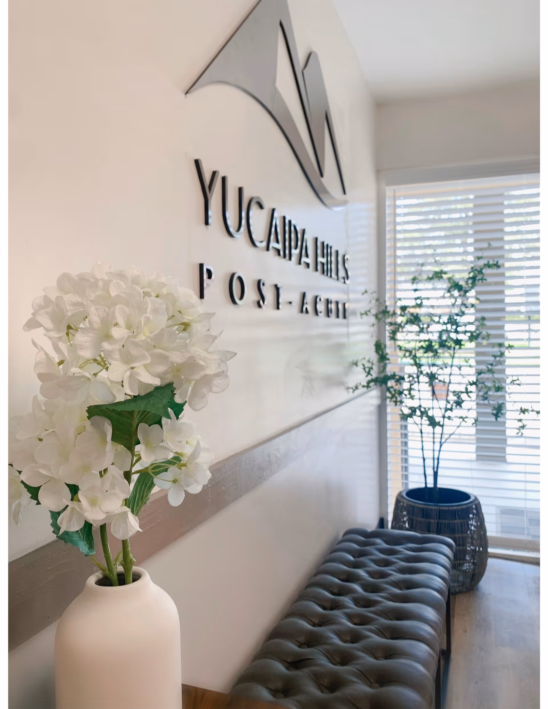 Reception area with white hydrangea bouquet, tufted bench, and Calimesa Post Acute sign.