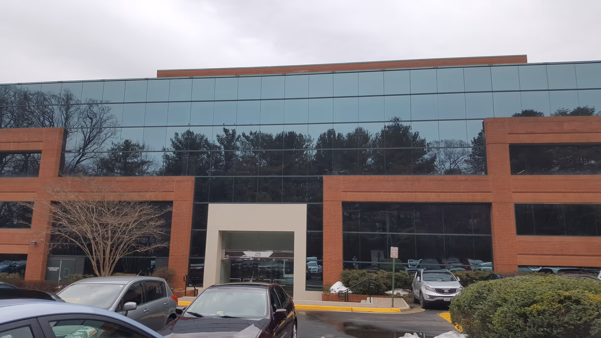 Brick-and-glass office building with a central entrance and parked cars in front.