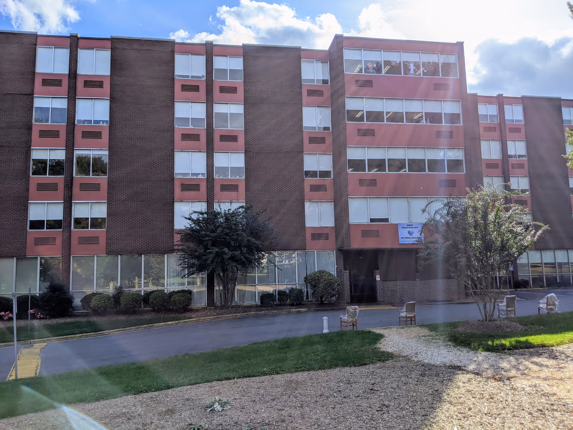 Exterior multi-story brick senior living building with landscaping and chairs.