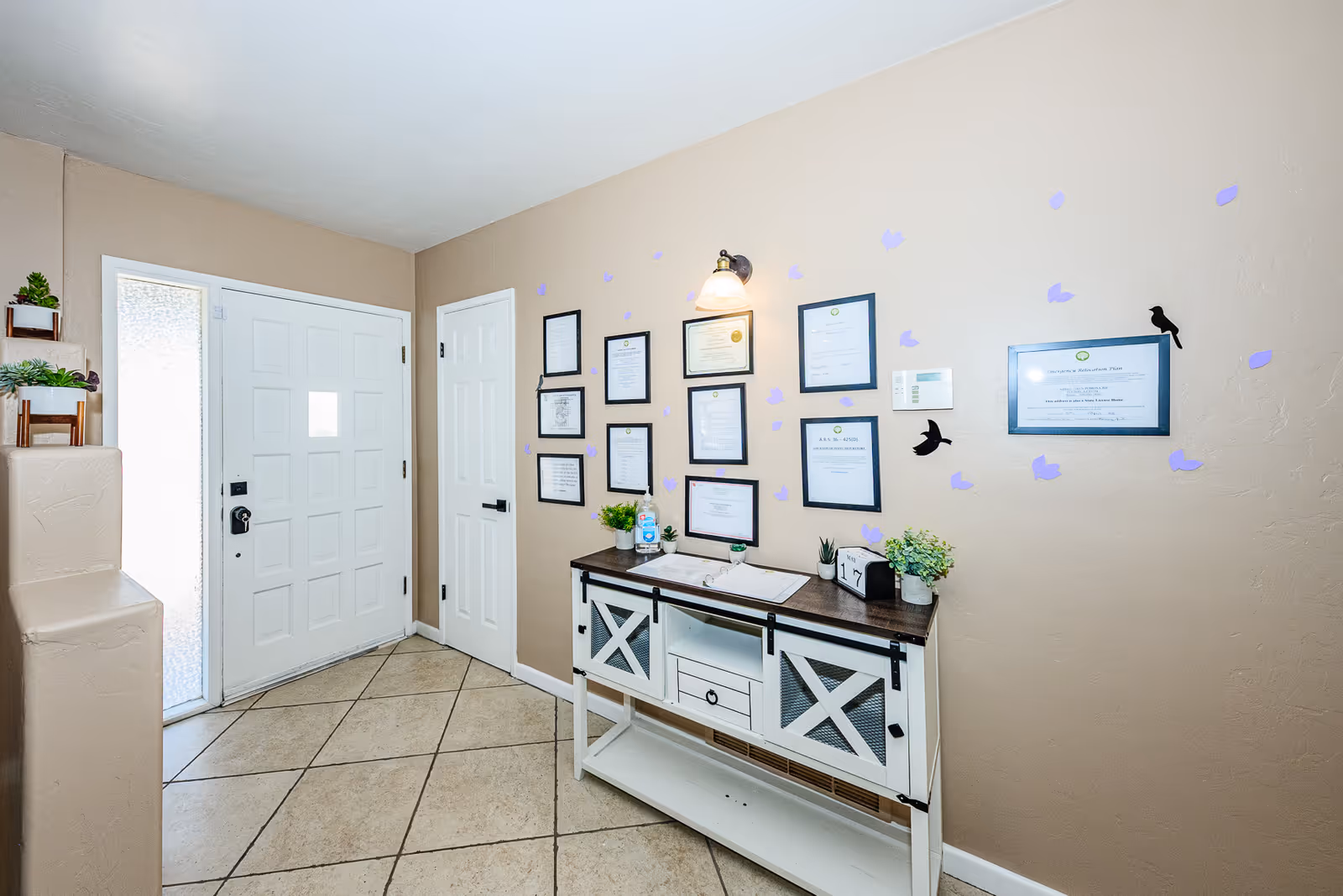 Beige entry hallway with framed certificates on the wall and a white console table.