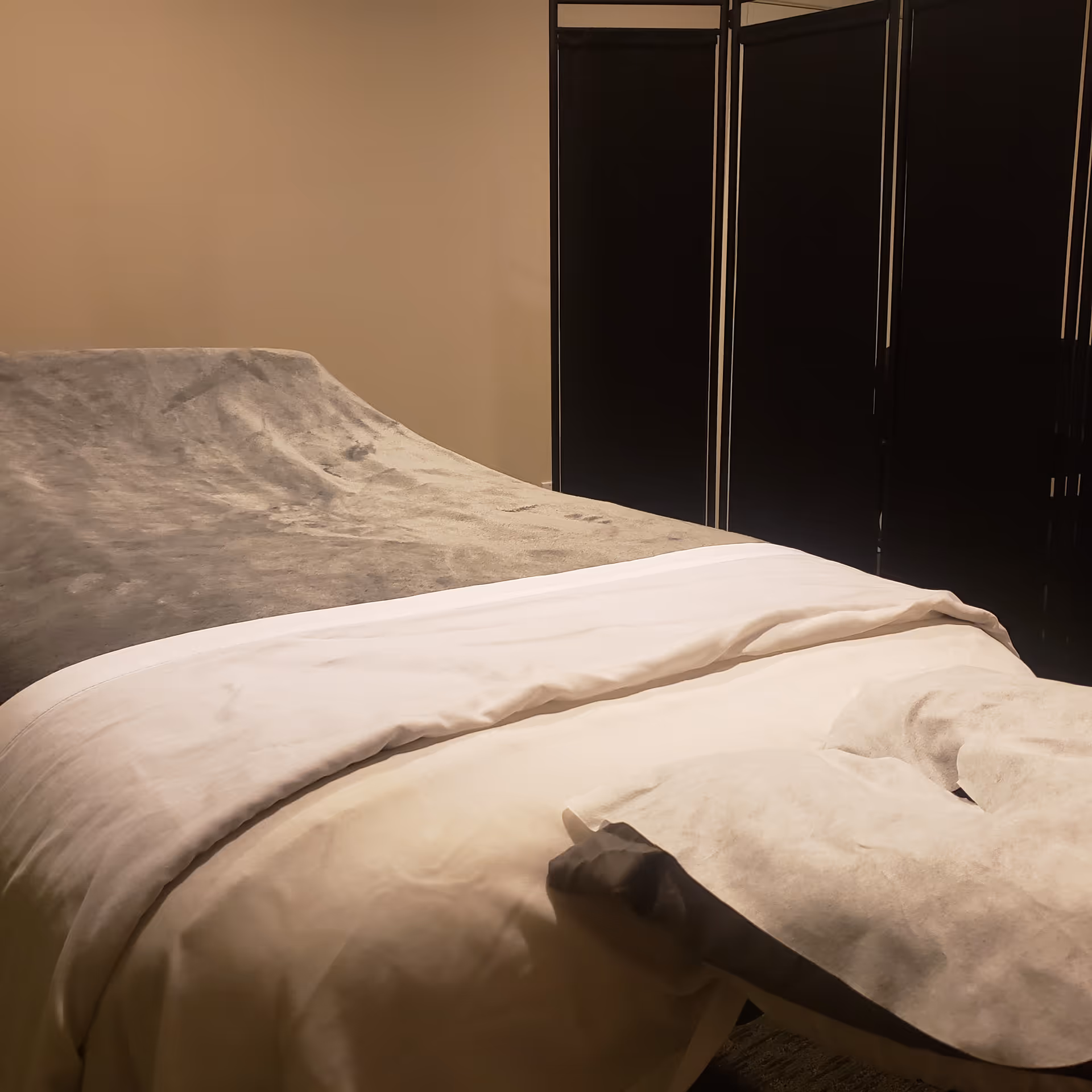 Neatly made bed with white sheets and gray blanket in a bedroom with dark wardrobes.