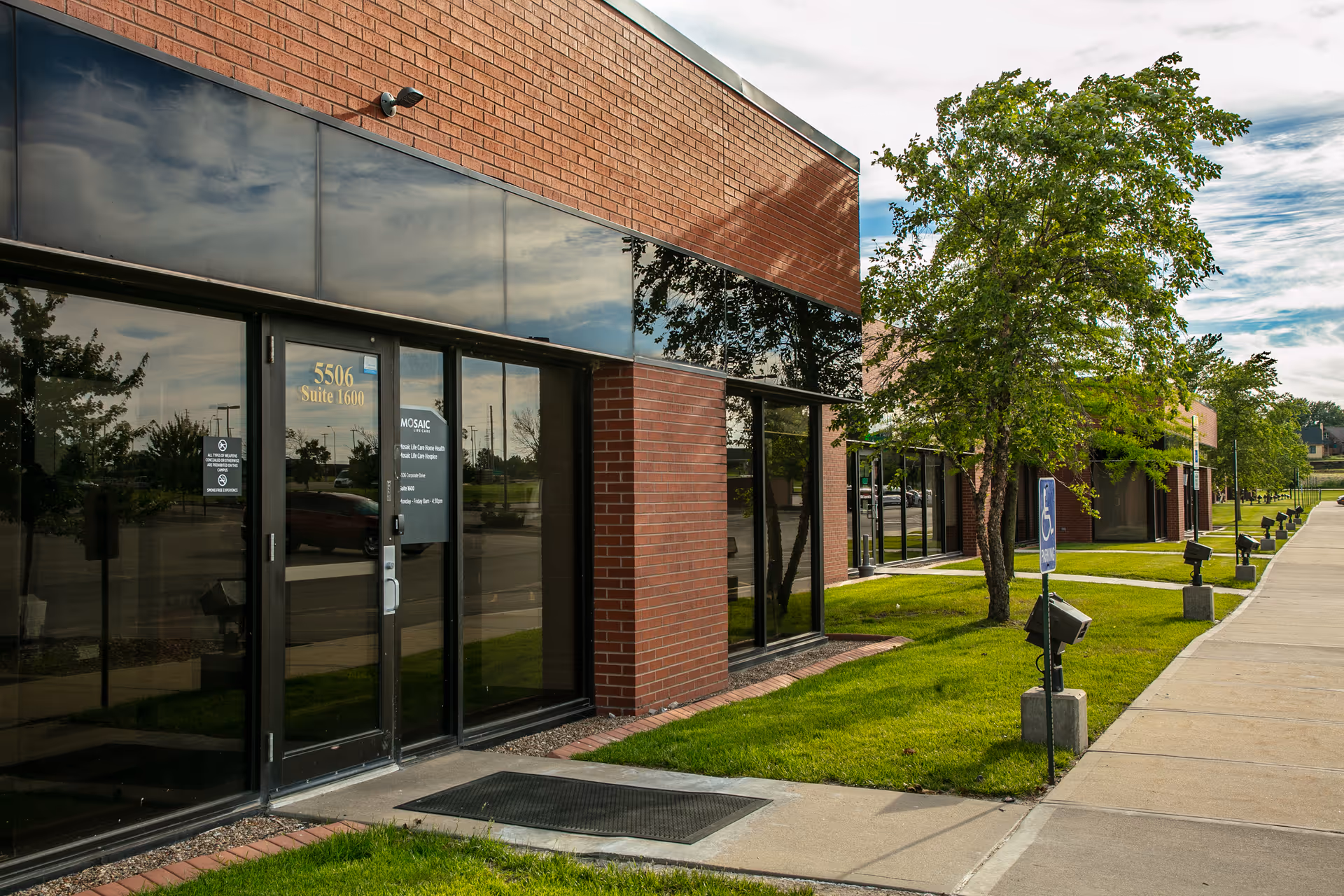 Exterior view of Mosaic Life Care Hospice building with brick facade, glass doors, and sidewalk.