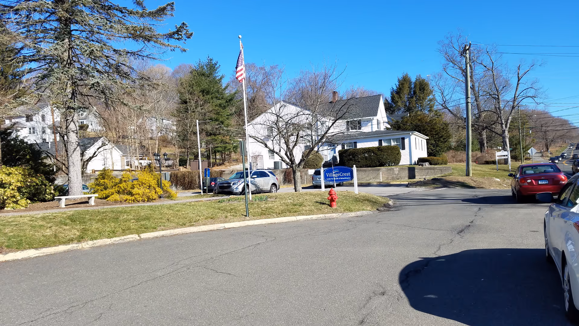 Street view of Village Crest Center for Health and Rehabilitation with flag, sign, and parked cars.