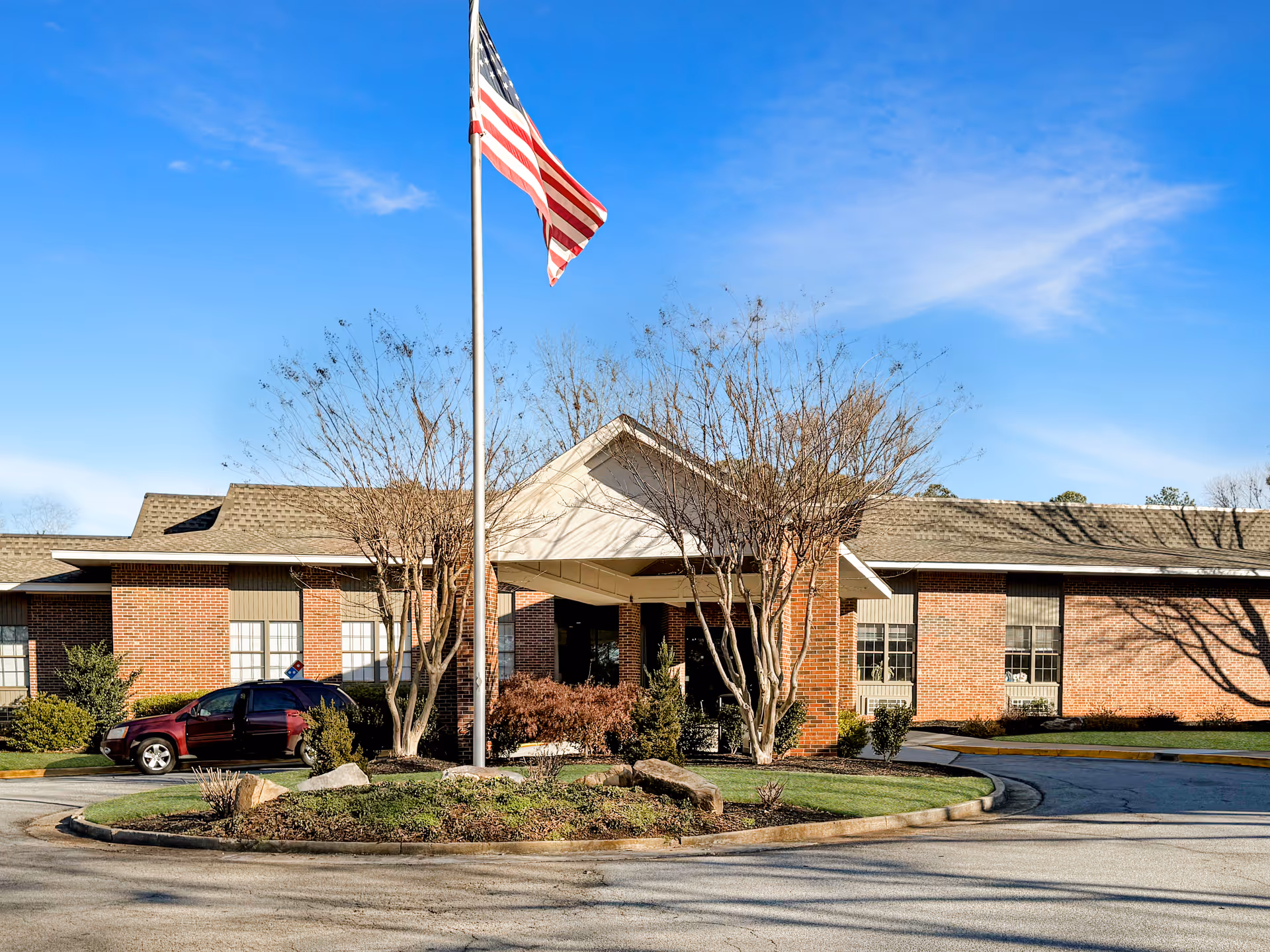 Brick senior living building facade with flagpole and landscaping in front.