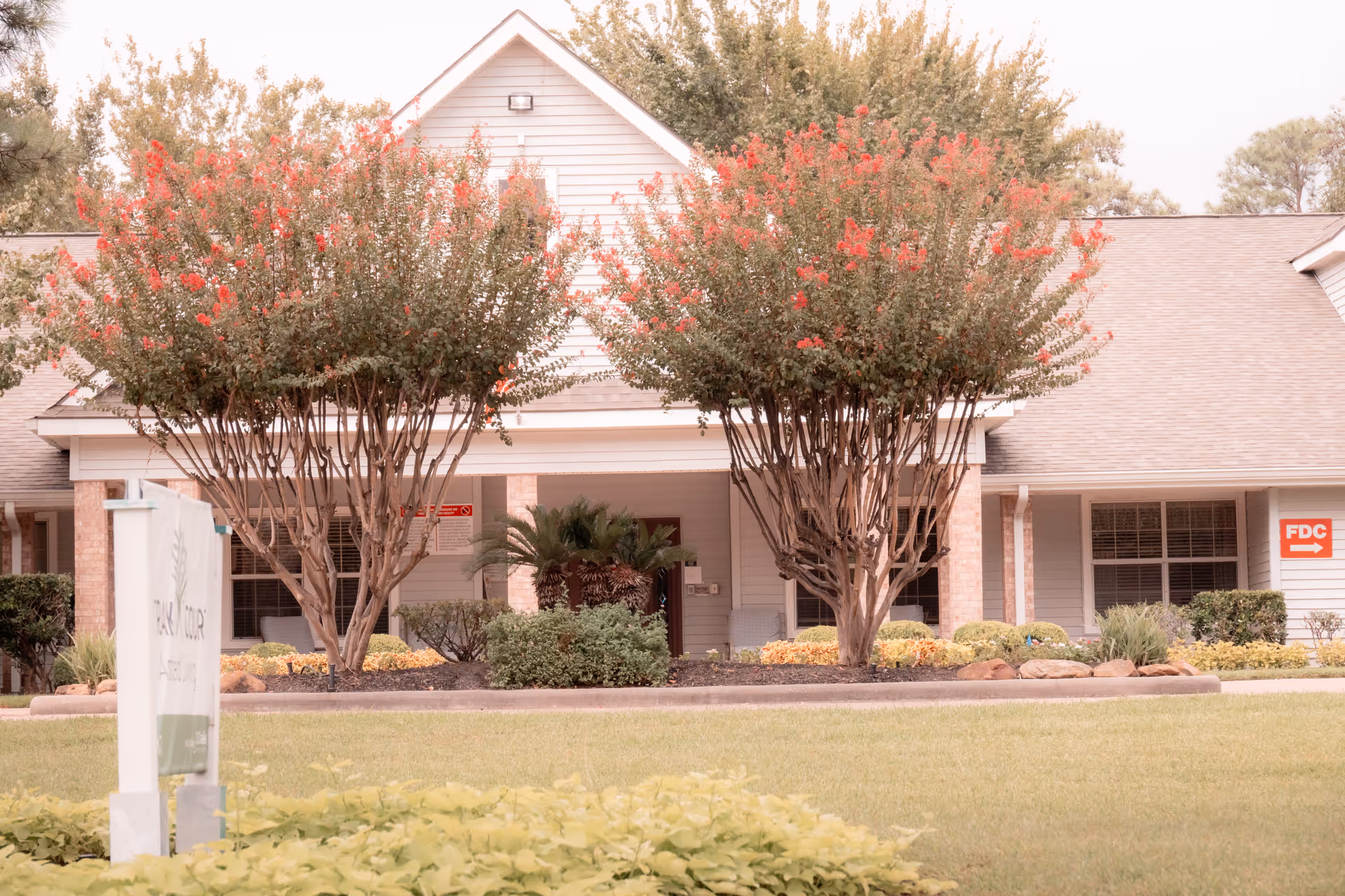 Front exterior of the Strake Court building with a landscaped lawn, two flowering trees flanking the entrance and a small sign in the front yard.