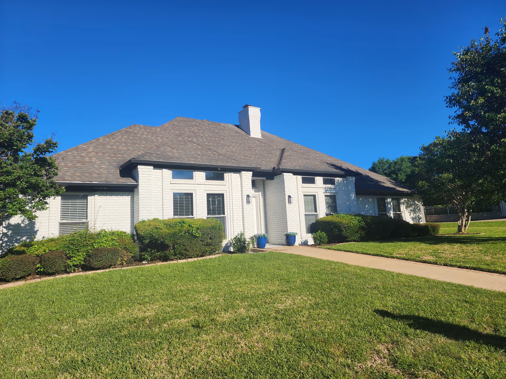 White brick building with manicured lawn, blue planters, and clear blue sky.