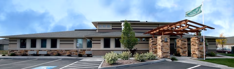 Single-story assisted living building exterior with a covered stone-column entrance, parking spaces and landscaped front.