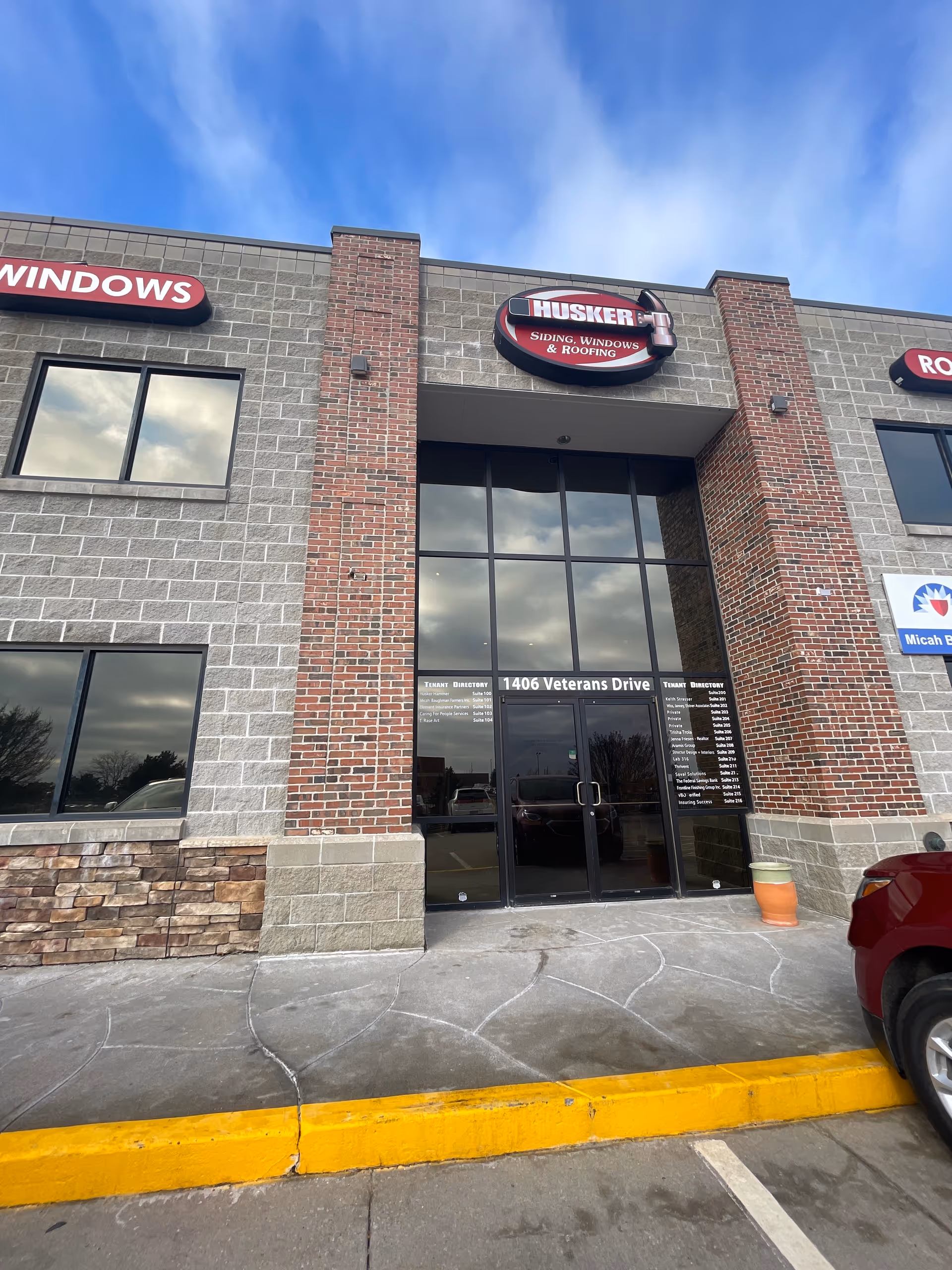 Front entrance of a brick building with large glass doors and Husker Siding sign.