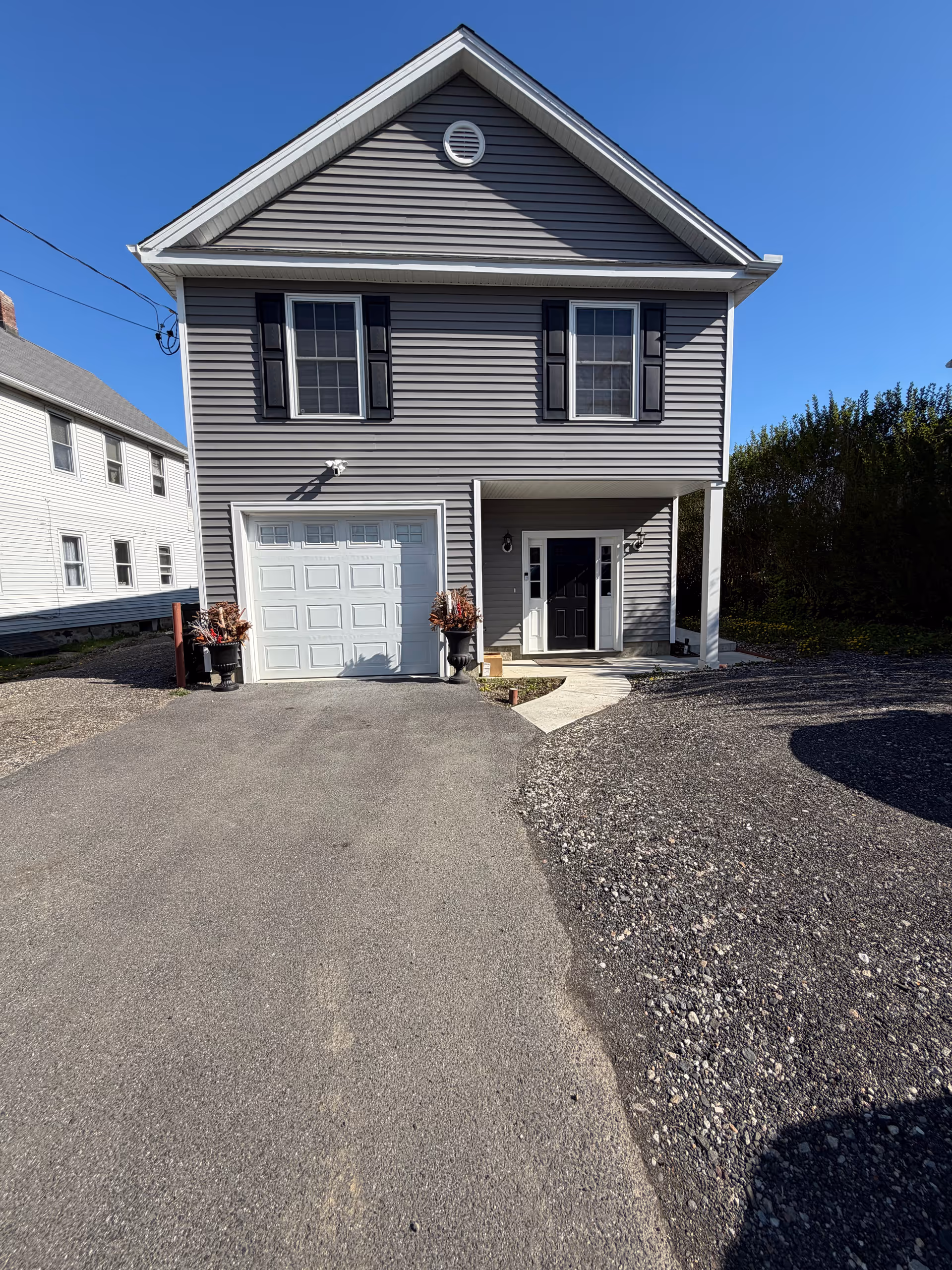 Gray two-story house with garage, front porch, and gravel driveway.