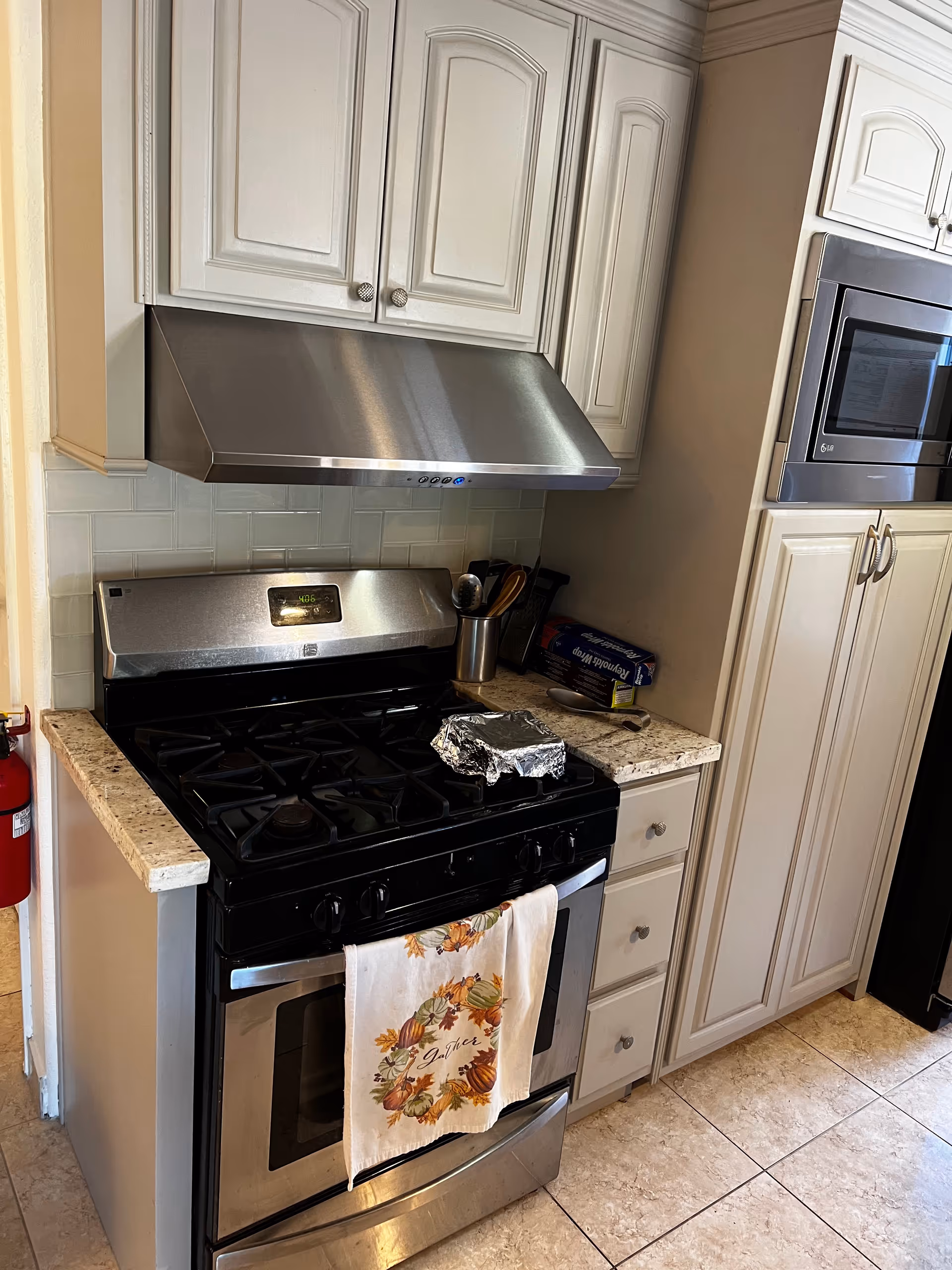 A compact kitchen featuring a stainless-steel stove, range hood, microwave, and white cabinets.