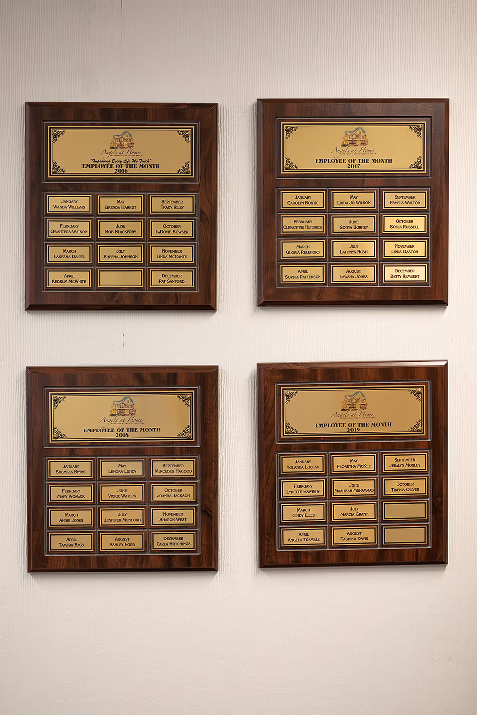 Four wooden wall plaques listing Employee of the Month mounted in a hallway.