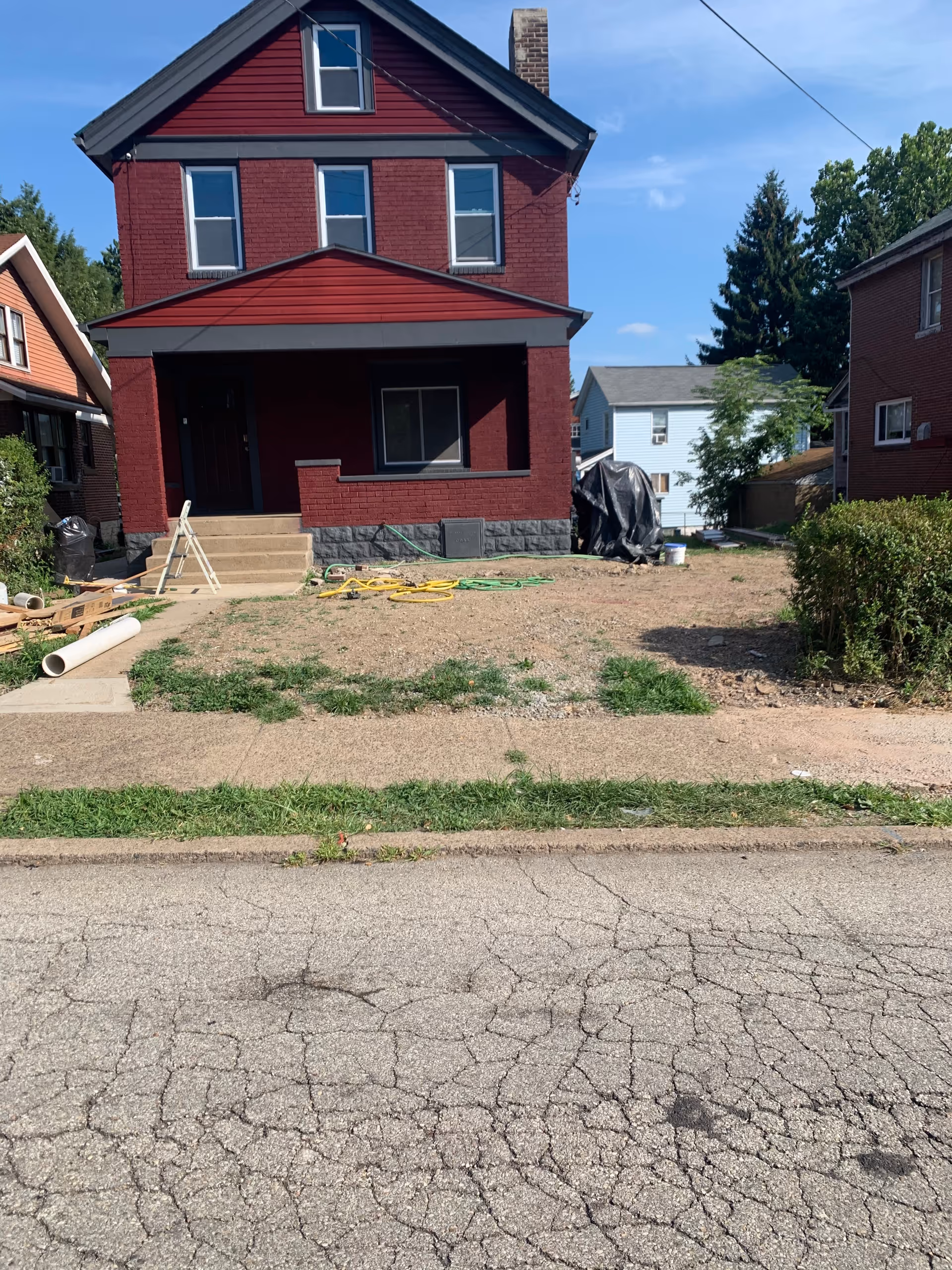 A red brick two-story house under renovation with tools and hoses in the front yard.