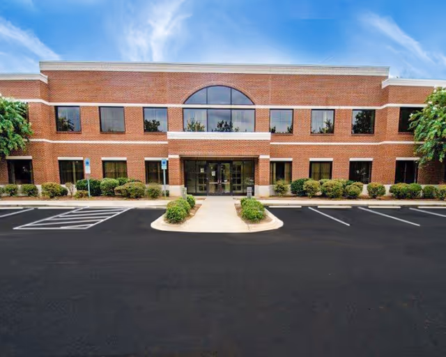 Exterior view of a brick senior living facility with a central entrance and parking area.