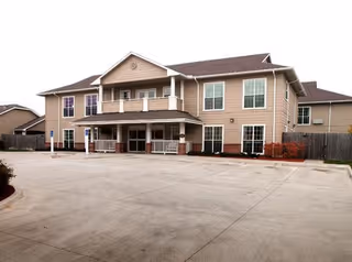Exterior view of a two-story beige assisted living building with a front entrance and parking.