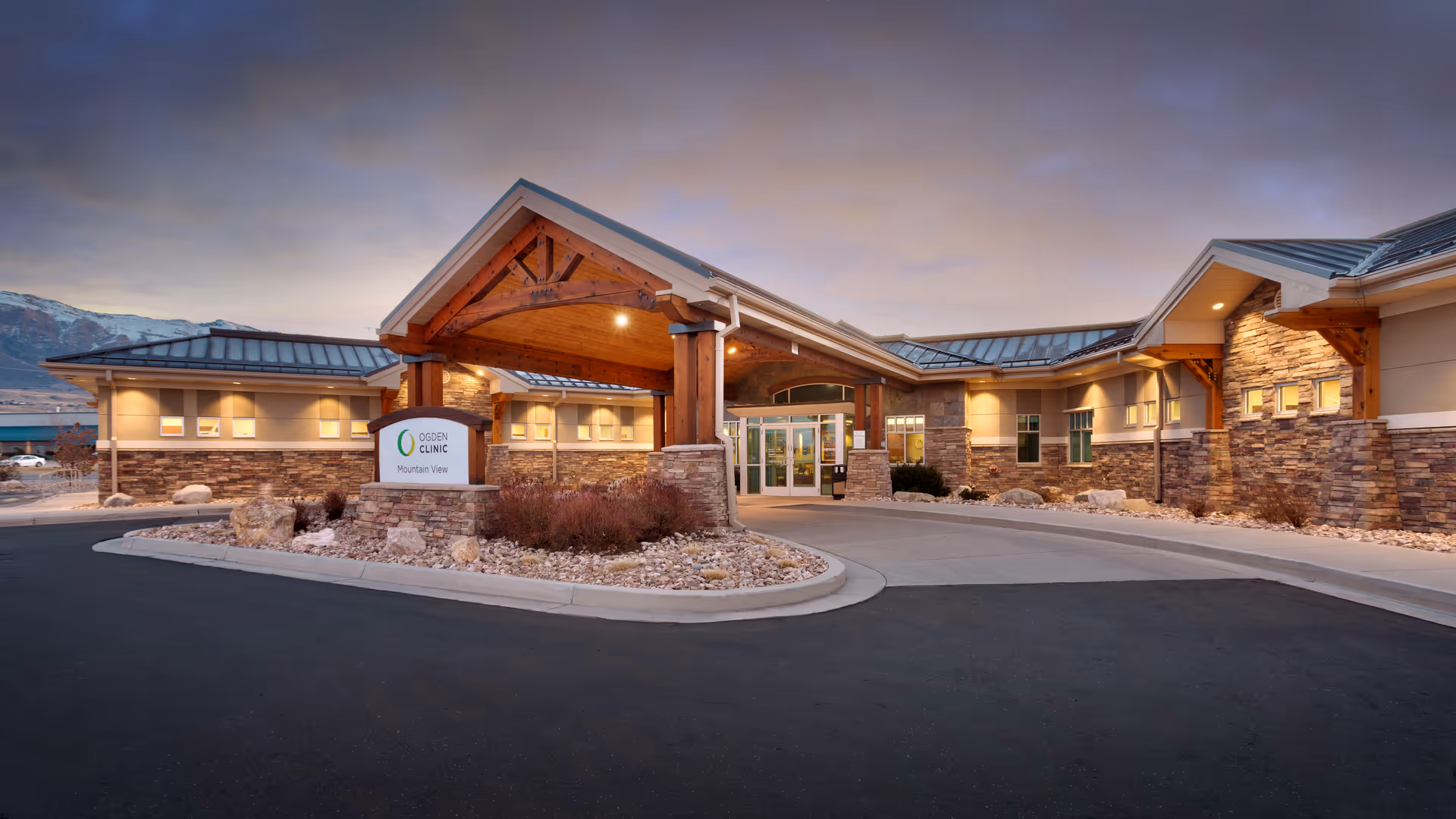 Stone-clad clinic exterior with wooden entrance canopy and landscaped driveway at sunset.