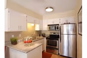 A compact kitchen with white cabinets, stainless steel fridge, microwave, sink, and countertop.