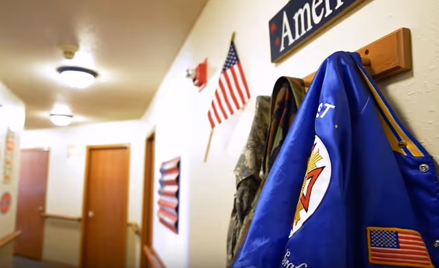 Interior hallway in a senior living facility with coats, flags, and doors.