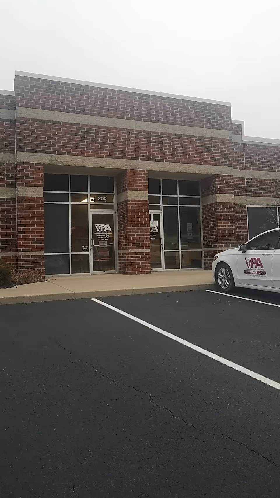 Exterior view of a brick medical office entrance with glass doors and a parked car.