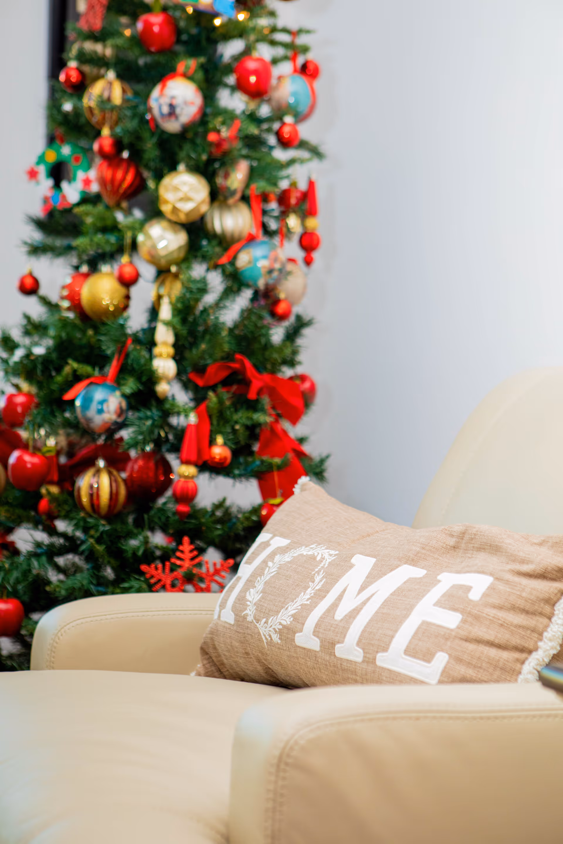 Beige living room featuring a decorated Christmas tree and a beige sofa with 'HOME' pillow.