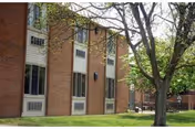 Brick senior living building exterior with windows, trees, and a green lawn.